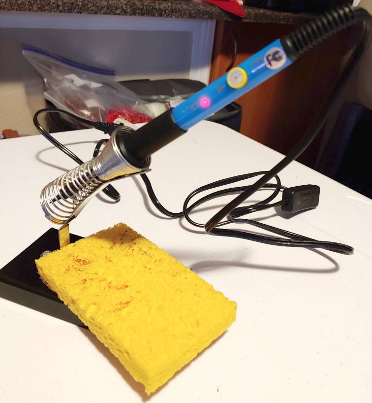 Soldering iron sitting in its stand with a large kitchen sponge.