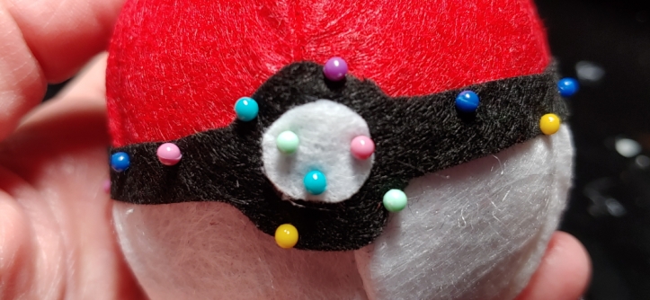 Gluing the center accents of a Pokeball and adding pressure with small pins (the round colorful dots)