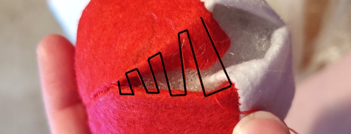 Showing how a ladder stitch is sewn on a plush pokeball. A black line zigzags between the open red section of the pokeball.