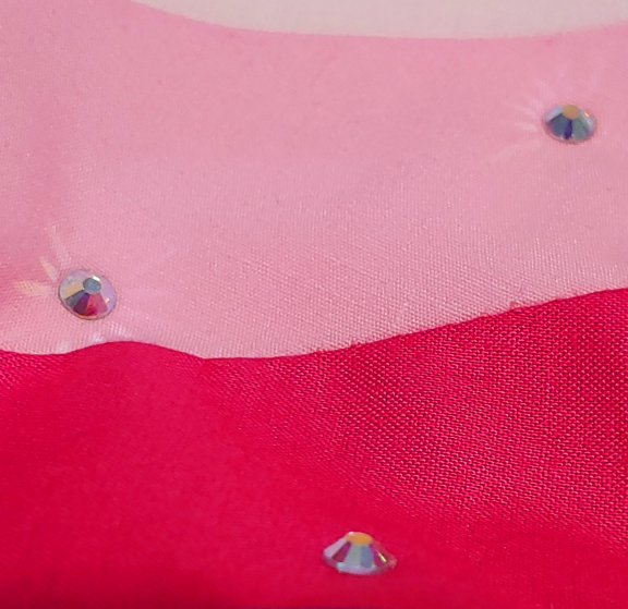 Several faceted rhinestones on bright pink fabric. they're casting light out on the surrounding fabric in beams