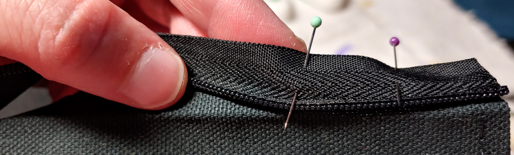 Pinning the zipper to the fabric. The teeth are aligned with the ironed fold of the fabric.