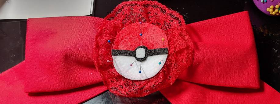Pinning a felt pokeball accent to a large hair bow. Pinning at angles like this creates enough pressure to make this stick. The pokeball is pinned with multiple small colored dots, which are the heads of very small pins.