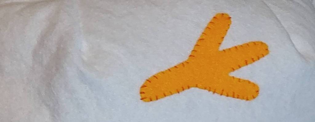 A chicken foot sewn on with a whip stitch. The foot is orange with darker orange stitches around the border